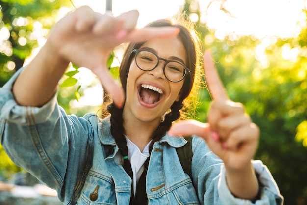 Portrait d'une jeune étudiante souriante et souriante qui crie et qui porte des lunettes à l'extérieur dans un parc naturel.