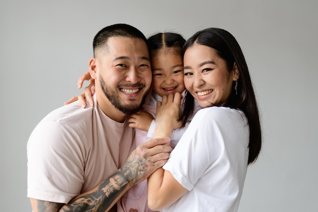 Photo portrait d'une jeune famille asiatique joyeuse avec sa fille regardant la caméra isolée sur le gris