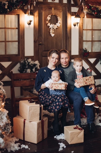 Portrait de jeune famille avec deux enfants se blottir sur un banc avec des cadeaux de Noël