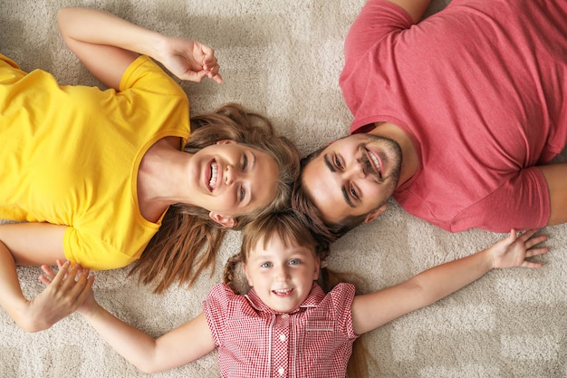 Portrait de jeune famille heureuse allongée sur un tapis à la maison