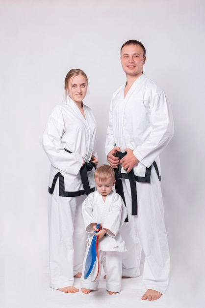 Portrait de jeune famille heureuse en uniforme d'arts martiaux debout sur blanc