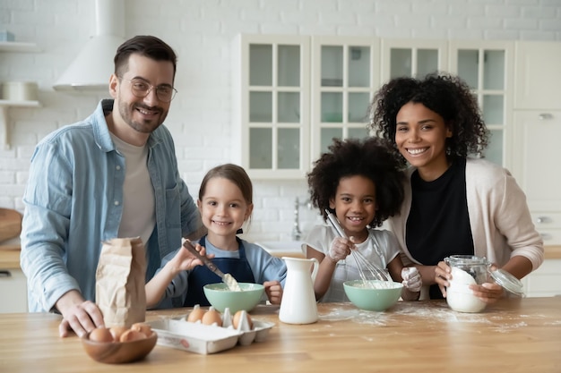 Portrait d'une jeune famille multiraciale heureuse avec de petites filles préparent des biscuits dans la cuisine ensemble des parents souriants avec de petites filles multinationales les enfants s'amusent à cuisiner le petit déjeuner à la maison