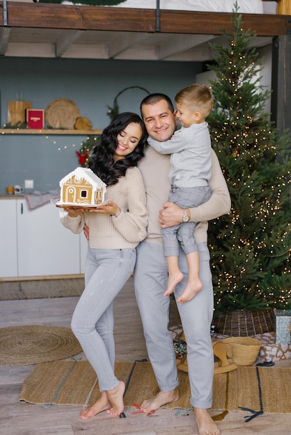 Photo portrait d'une jeune famille souriante avec une maison en pain d'épice une tradition familiale pendant les vacances de noël