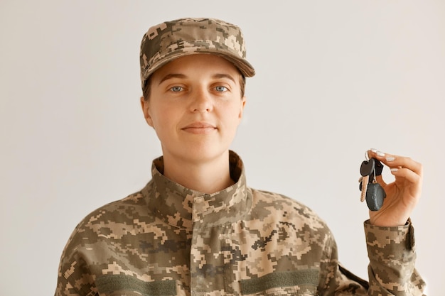 Portrait d'une jeune femme adulte confiante portant un uniforme de camouflage et une casquette debout et regardant la caméra et tenant les clés d'un nouvel appartement