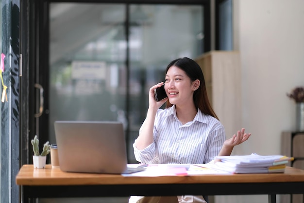 Portrait de jeune femme d'affaires asiatique parler sur smartphone écrire ordinateur portable ordinateur portable dans le bureau à domicile