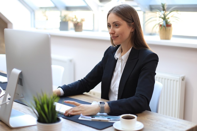 Portrait d'une jeune femme d'affaires blonde à l'aide d'un ordinateur au bureau.