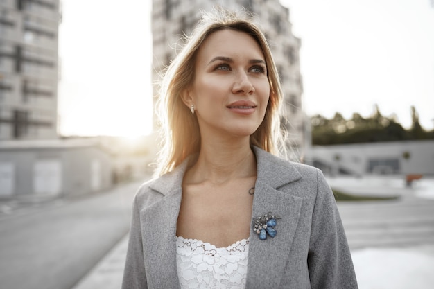 Portrait de jeune femme d'affaires blonde en costume gris marchant dans la ville