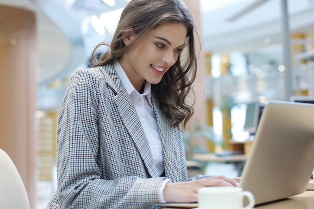 Portrait d'une jeune femme d'affaires brune utilisant un ordinateur portable au bureau.