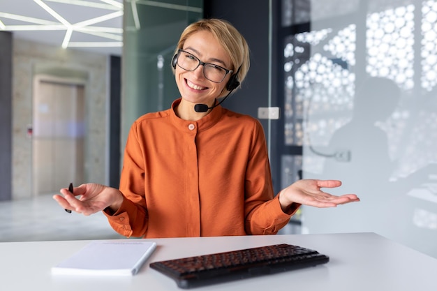 Portrait d'une jeune femme d'affaires dans un casque assis au bureau à la table et parlant à