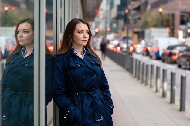 Portrait de jeune femme d'affaires dans un manteau bleu, sur fond de grande ville.