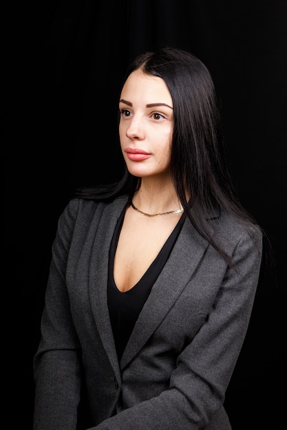 Portrait de jeune femme d'affaires dans une veste grise sur fond noir.