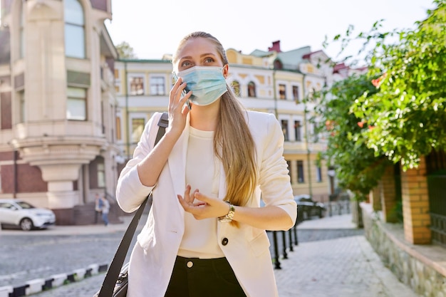 Portrait d'une jeune femme d'affaires employée de bureau dans un masque de protection médicale parlant sur un téléphone portable en plein air sur fond de rue de la ville Épidémie pandémie personnes de soins de santé et concept d'entreprise
