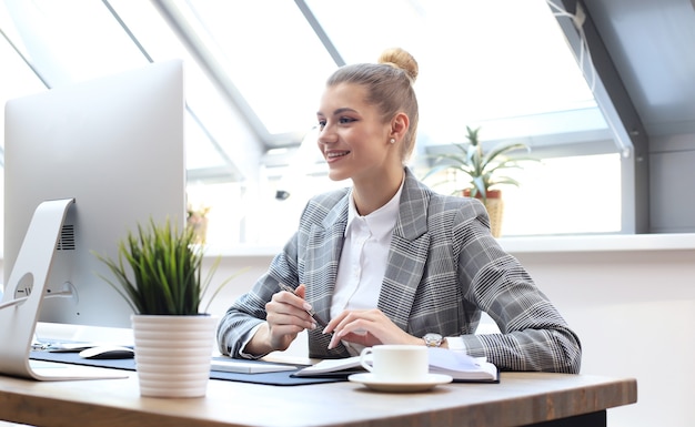 Portrait d'une jeune femme d'affaires joyeuse assise à la table au bureau et regardant la caméra.