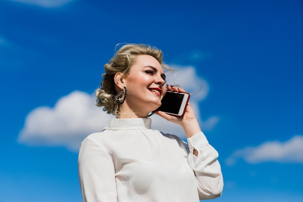 Portrait d'une jeune femme d'affaires avec téléphone, ordinateur portable, tablette, café en plein air. Fille blonde en gants de caoutchouc bleu.