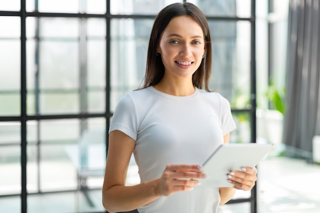 Portrait de jeune femme d'affaires tenant un pavé tactile tout en se tenant dans l'intérieur de l'espace de bureau moderne