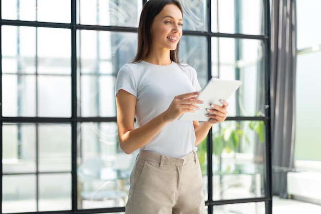 Portrait de jeune femme d'affaires tenant un pavé tactile tout en se tenant dans l'intérieur de l'espace de bureau moderne