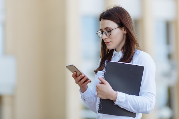 Portrait jeune femme d'affaires vêtu d'une chemise blanche à l'aide de smartphone par les portes.