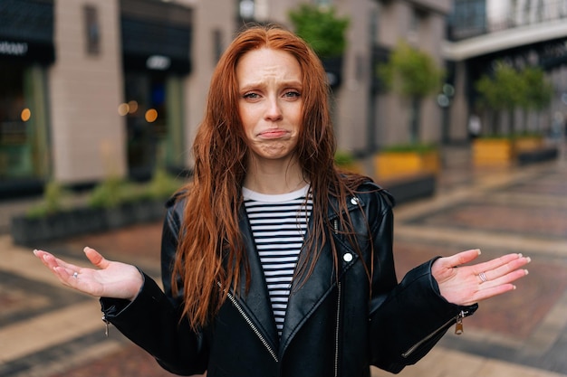 Portrait d'une jeune femme affolée avec de longs cheveux roux debout avec des cheveux ébouriffés après avoir été pris sous une pluie froide d'automne en train de pleurer en regardant la caméra