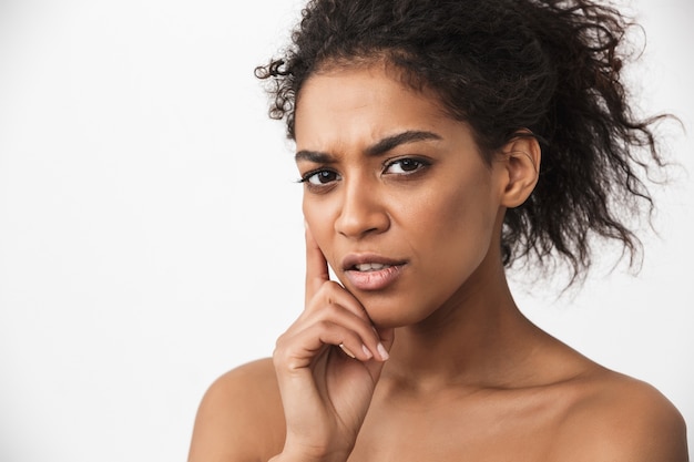 Portrait d'une jeune femme africaine assez sérieuse posant isolé sur un mur blanc.