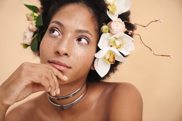 Portrait de jeune femme afro-américaine aux taches de rousseur à moitié nue avec des fleurs dans les cheveux