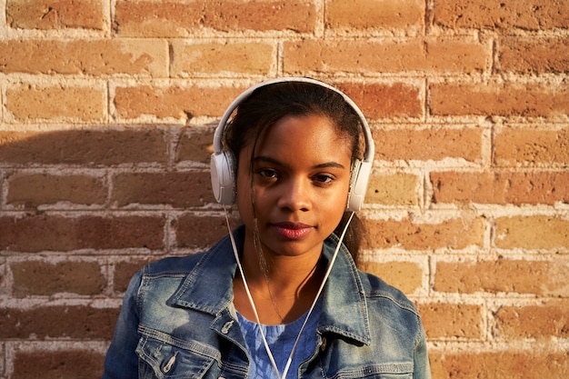 Portrait de jeune femme afro-américaine avec un casque d'écoute de la musique devant un mur de briques.