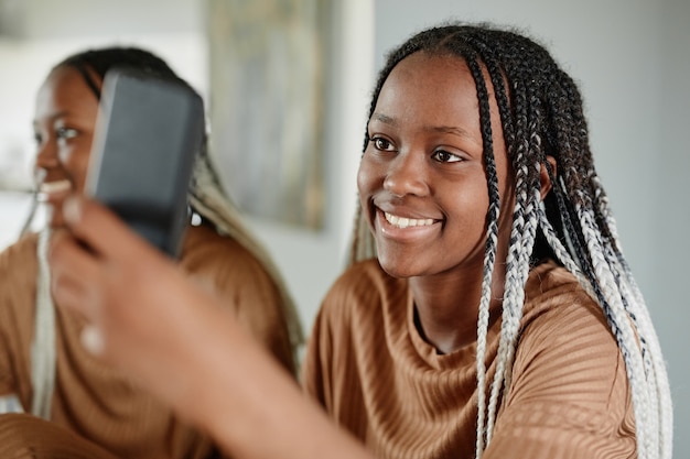 Portrait d'une jeune femme afro-américaine discutant avec des amis via un smartphone et souriant