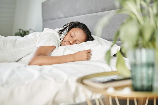 Portrait de jeune femme afro-américaine dormant sur des draps blancs dans l'espace de copie du matin