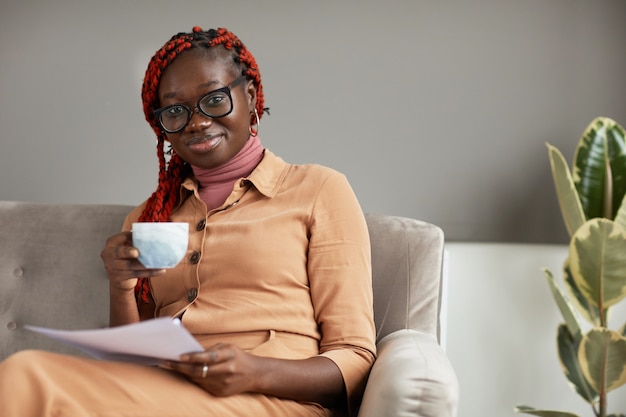 Portrait de jeune femme afro-américaine tenant une tasse de café et souriant à la caméra tout en profitant du travail du bureau à domicile, copiez l'espace