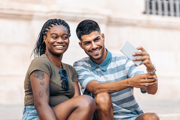 Portrait d'une jeune femme afro et d'un homme de race blanche prenant un selfie avec le mobile dans la rue