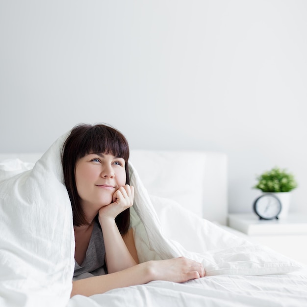 Portrait de jeune femme allongée dans son lit et pensant ou rêvant de quelque chose à la maison