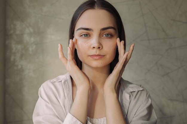 Portrait de jeune femme appliquant une crème hydratante pour les yeux sur le visage pendant la routine de beauté des soins de la peau