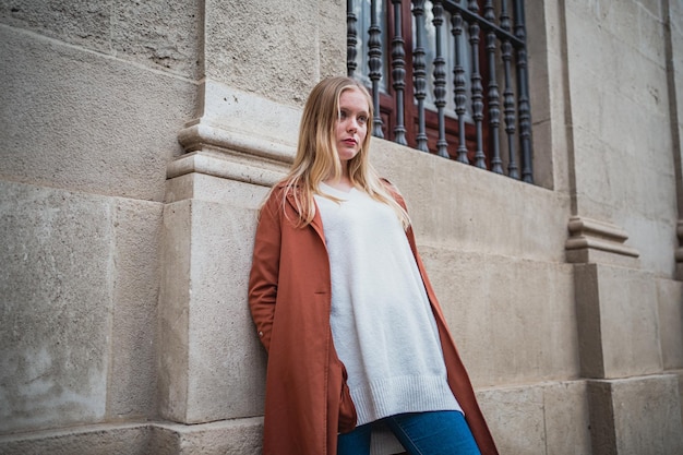 Portrait de jeune femme appuyée contre le mur de la ville Elle porte un manteau orange