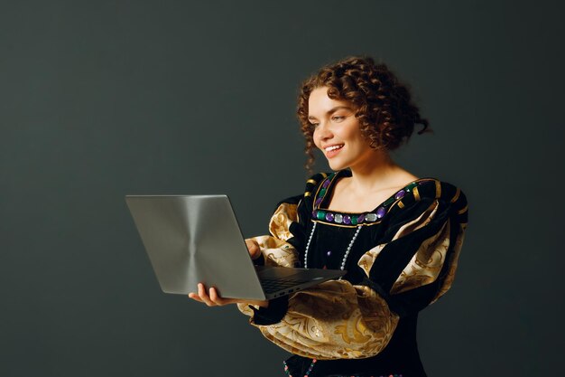 Portrait d'une jeune femme aristocratique vêtue d'une robe médiévale travaillant sur un ordinateur portable
