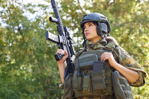 Portrait de jeune femme avec une arme en tenue militaire à l'extérieur