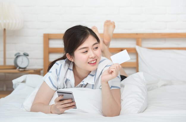 Portrait de jeune femme asiatique allongée sur le lit à l'aide d'un téléphone mobile intelligent numérique