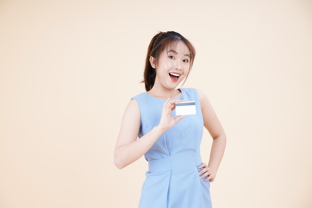 Portrait d'une jeune femme asiatique belle et joyeuse utilisant une carte de crédit pour payer en ligne isolée sur fond