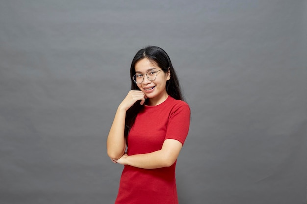 Portrait jeune femme asiatique brune dans une robe rouge bras croisés sur la poitrine et déterminé posé souriant avec confiance tourné en studio isolé sur fond gris