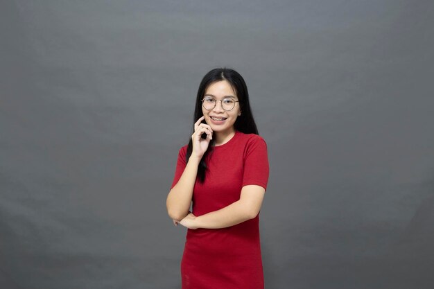 Portrait jeune femme asiatique brune dans une robe rouge bras croisés sur la poitrine et déterminé posé souriant avec confiance tourné en studio isolé sur fond gris