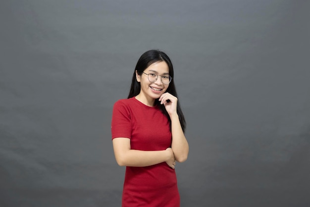 Portrait jeune femme asiatique brune dans une robe rouge bras croisés sur la poitrine et déterminé posé souriant avec confiance tourné en studio isolé sur fond gris