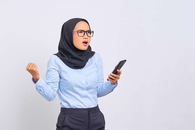 Portrait de jeune femme asiatique choquée tenant un téléphone portable et regardant de côté avec la bouche ouverte isolée sur fond blanc