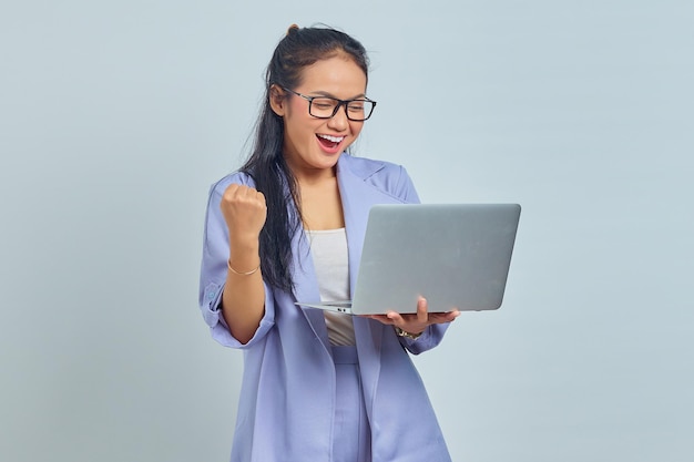 Portrait d'une jeune femme asiatique excitée debout tenant un ordinateur portable et célébrant la chance pour un nouvel emploi isolé sur fond blanc