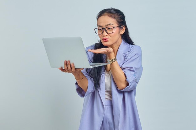 Portrait d'une jeune femme asiatique gaie debout à l'aide d'un ordinateur portable et envoyant un baiser aérien à son petit ami pendant un appel vidéo isolé sur fond blanc