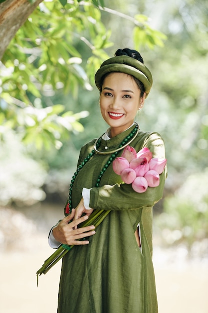 Portrait d'une jeune femme asiatique heureuse en costume national posant avec des fleurs de lotus