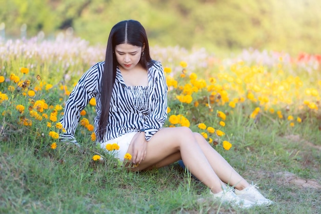 Portrait d'une jeune femme asiatique heureuse voyageuse avec une robe à motif noir et blanc profitant d'un champ de fleurs en fleurs jaunes dans le jardin naturel de en Thaïlande