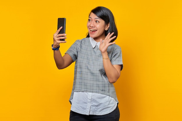 Portrait d'une jeune femme asiatique joyeuse et excitée utilisant un téléphone portable prendre un selfie sur fond jaune