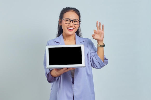 Portrait d'une jeune femme asiatique joyeuse montrant un écran d'ordinateur portable vierge et montrant un signe correct isolé sur fond blanc