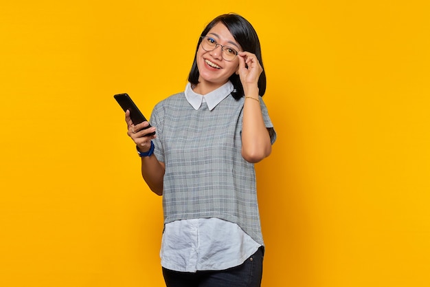 Portrait d'une jeune femme asiatique joyeuse tenant un smartphone et des lunettes regardant la caméra