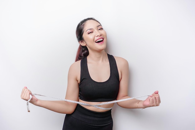 Portrait d'une jeune femme asiatique joyeuse en vêtements de sport mesurant la taille avec du ruban adhésif se sentant heureuse de perdre du poids à la maison Sport de mode de vie sain et concept de régime amincissant