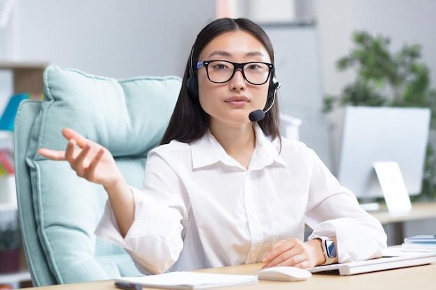 Portrait d'une jeune femme asiatique à lunettes et écouteurs avec un microphone assis au bureau