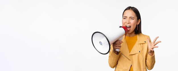 Portrait d'une jeune femme asiatique manifestant criant dans un mégaphone et protestant debout confiant sur fond blanc